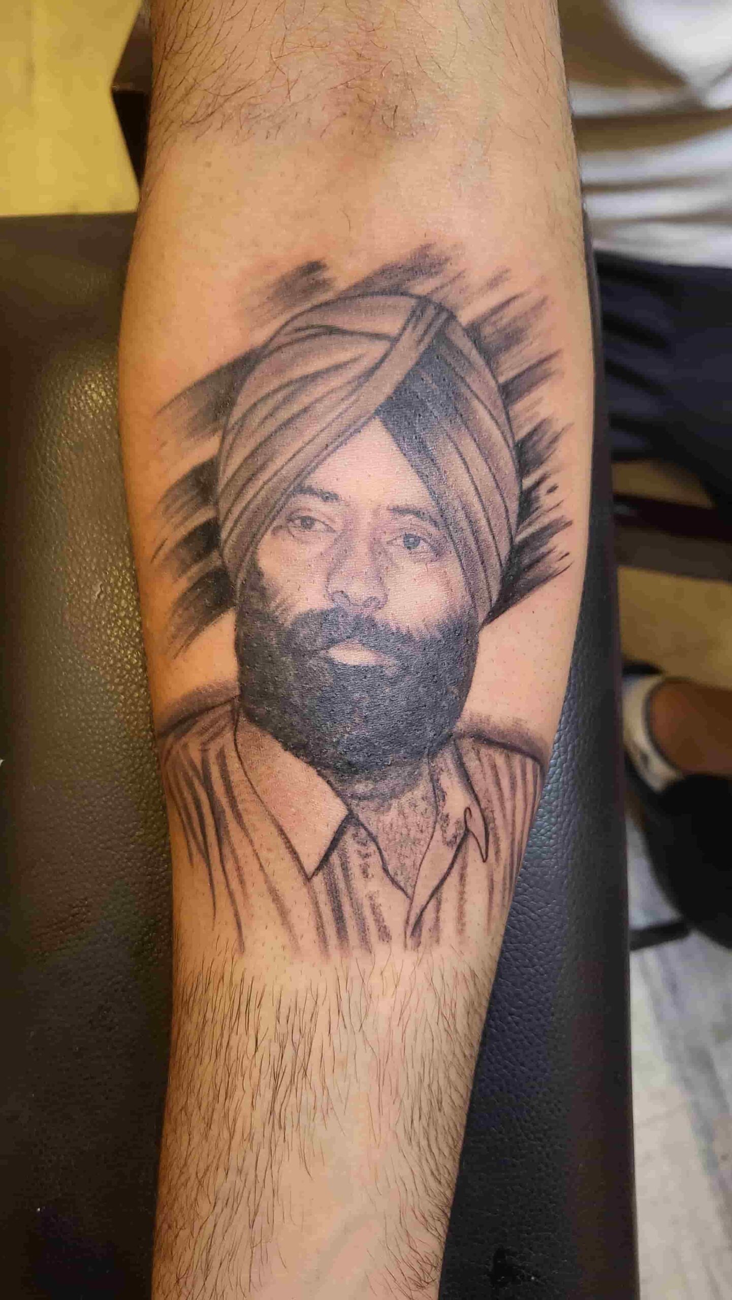 Black-and-grey portrait tattoo of a turbaned man on a client’s forearm
